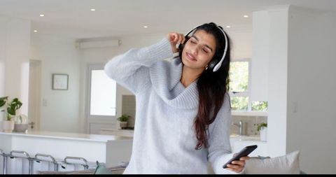 Relaxed woman enjoying music on headphones in modern kitchen