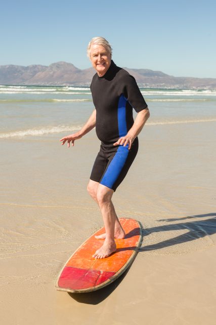 Senior man enjoying surfing at the beach on a sunny day. Ideal for use in advertisements promoting active lifestyles for seniors, travel brochures, health and fitness campaigns, and retirement community promotions.