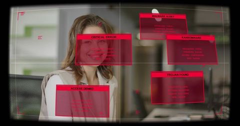 Smiling woman sitting at office workstation with red cybersecurity alert overlays