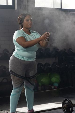 African american woman chalking hands preparing to lift barbell on sunlit gym platform