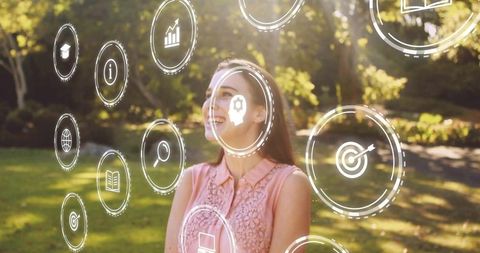 Smiling woman viewing augmented reality icons in sunlit park with digital learning overlay