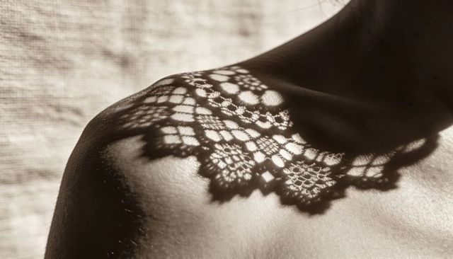 Lace shadow draping shoulder and clavicle in warm sunlight intimate pattern silhouette
