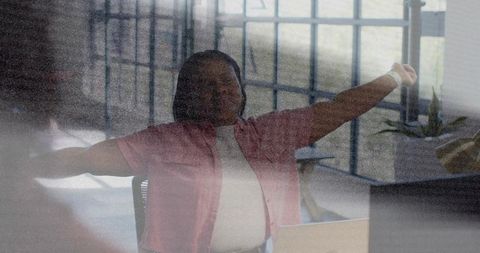 Woman stretching at desk in sunlit modern office with laptop and plants