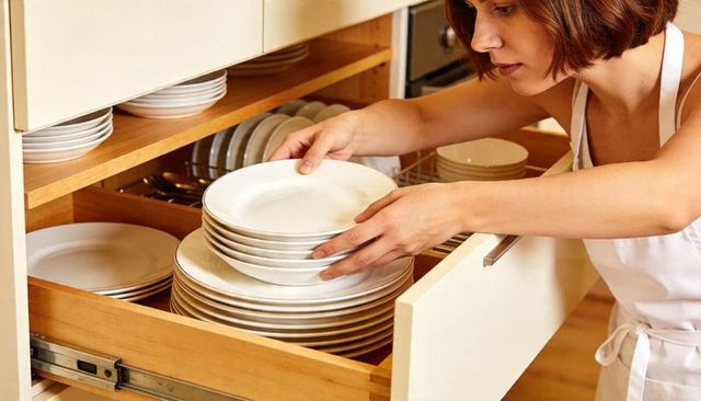 Woman organizing white dinner plates in wooden pull-out kitchen drawer home organization