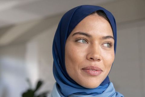 Contemplative muslim woman wearing layered blue hijab gazing in modern interior