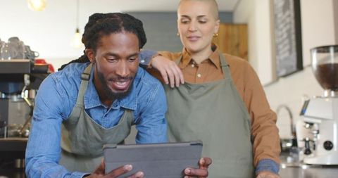 Black male and white female baristas collaborating over tablet in cozy cafe managing orders