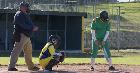 Amateur baseball batter preparing swing with catcher crouching and umpire at home plate