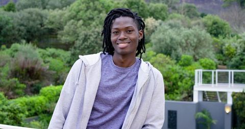 Smiling African American man leaning on balcony wearing hoodie with green hillside backdrop