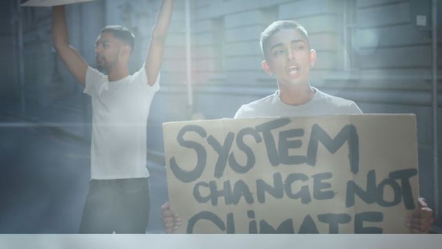 Individuals expressing strong sentiments for systemic change over climate policies. The scene illustrates diverse participants actively voicing their beliefs using handmade cardboard signs during a daylight protest. Ideal for campaigns promoting political awareness, community organizing, environmental changes, or minority voices in activism.