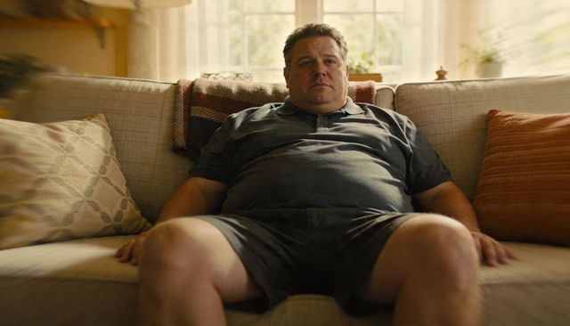 Middle-aged man slouching on sofa in sunlit cozy living room with woven blanket