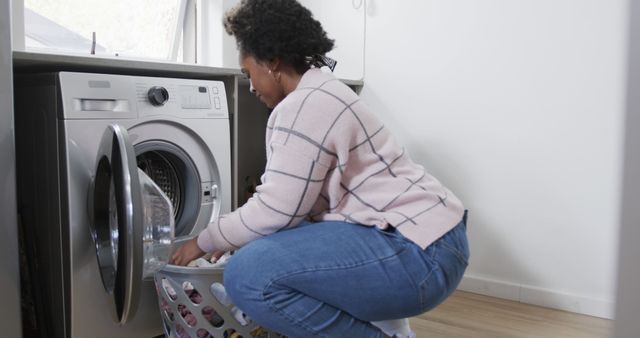 African american woman doing laundry in kitchen at home. Lifestyle, cleaning, hygiene and domestic life, unaltered.