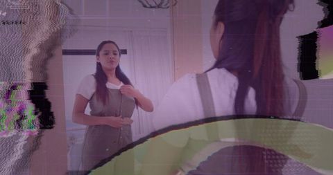 Young indian woman adjusting pinafore straps in mirror with retro digital glitch youthful
