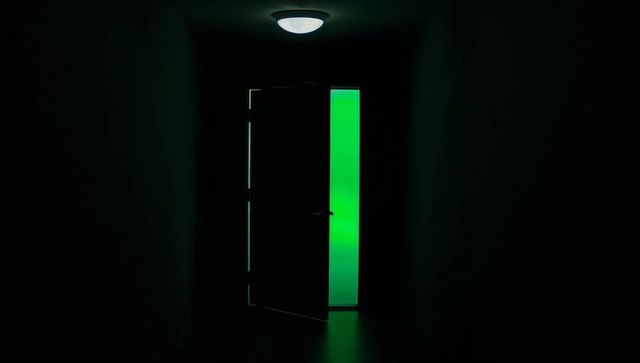 Partially Open Door Emitting Narrow Neon Green Light Along Dark Corridor