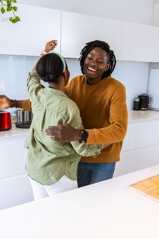 African american couple dancing and embracing in bright white modern kitchen