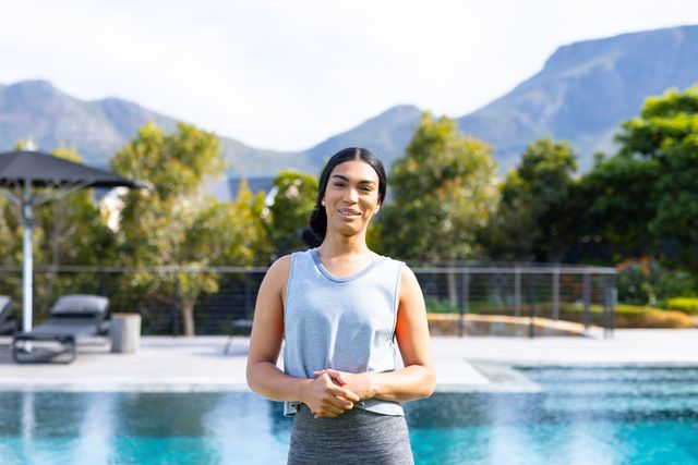 Portrait of happy, biracial gender fluid person smiling in sunny garden by pool, copy space. Healthy lifestyle, inclusivity and happiness concept.