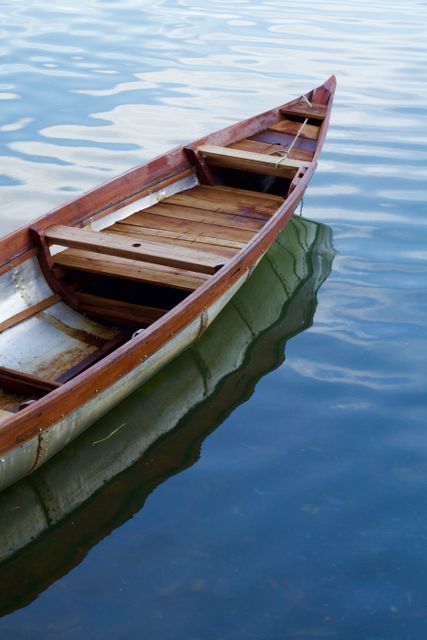 Empty wooden boat floating on calm water surface with clear reflection. Ideal for travel brochures, nature blogs, and relaxation themes. Perfect for showcasing serenity, peace, and traditional craftsmanship.
