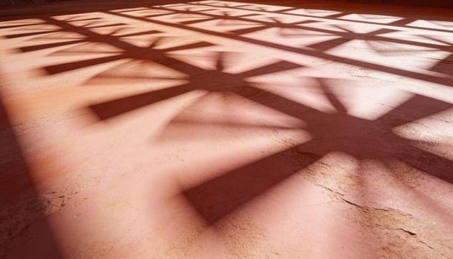 Lattice shadows casting over terracotta pink floor revealing cracked texture and geometry