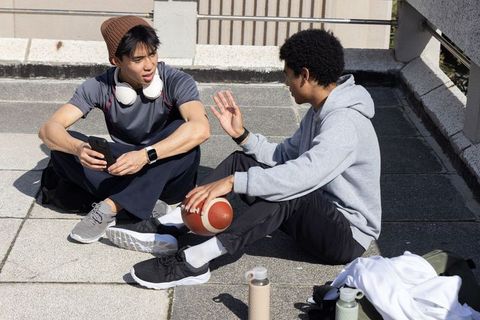 Rooftop friends chatting and holding smartphone and football in casual streetwear