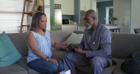 Home healthcare nurse measuring blood pressure for mature african american woman on sofa