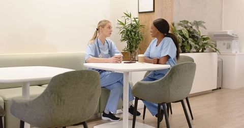 Nurses chatting and sharing coffee in clinic breakroom, modern staff lounge promoting teamwork
