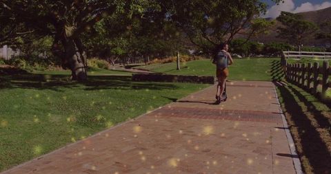 Woman riding scooter on sunny park path