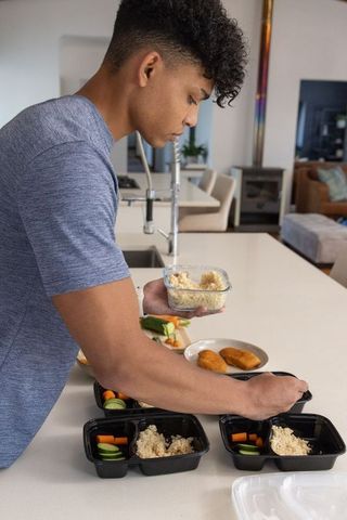 African american man preparing healthy meal prep boxes on modern kitchen island