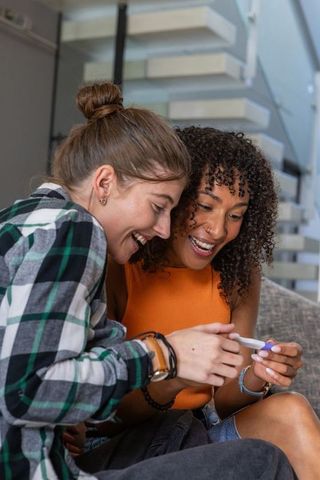 Joyous female couple celebrating positive pregnancy news at home