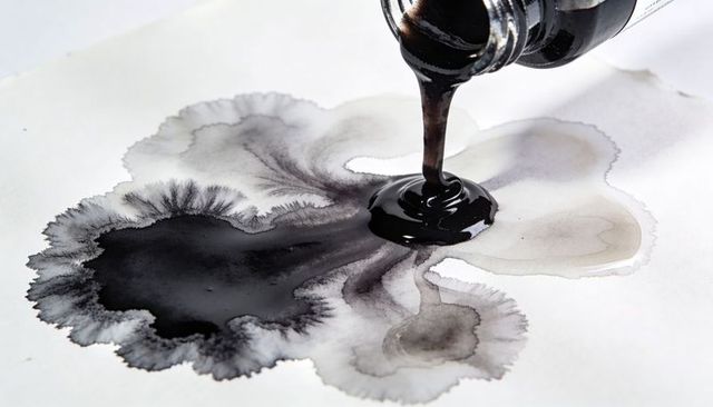 Pouring black ink forming organic watercolor blooms, glossy spill and fractal texture