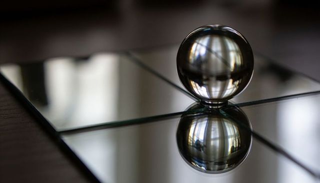 Crystal sphere creating inverted reflection on mirrored tile grid and tabletop symmetry