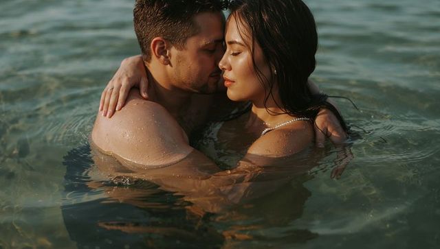 Sunlit couple embracing in shallow sea with beaded swimsuit strap romantic intimacy