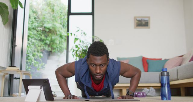 Happy african american man exercising in living room, using tablet. Spending quality time at home alone.