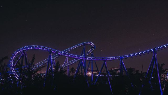 Illuminated roller coaster loops radiating purple led lights at night