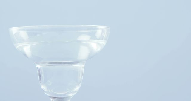 A clear glass with a unique design is set against a plain, light blue background, with copy space. Its simplicity and the monochrome palette make it ideal for minimalist aesthetics or showcasing glassware.
