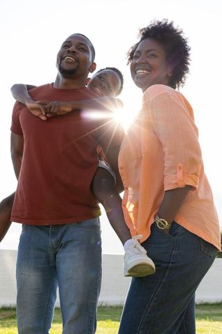 African american family enjoying sunny waterfront day with father carrying son on piggyback