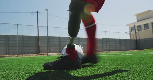 Close-up view of an athlete with a prosthetic leg kicking a soccer ball on a grass field. Can be used in campaigns promoting adaptive sports, inclusivity in athletics, and overcoming challenges. Ideal for articles or advertisements focused on resilience, sportsmanship, and motivation.