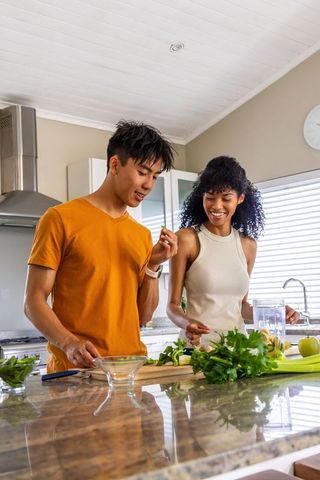 Asian man and african american woman preparing herbs and apples on kitchen island smiling