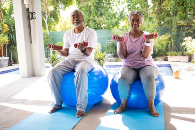 Senior couple lifting dumbbells while sitting on fitness balls in an outdoor yard. Ideal for promoting healthy lifestyles, senior fitness programs, wellness retreats, and active aging. Can be used in advertisements, health and fitness blogs, and retirement community brochures.