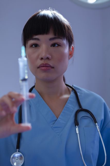 Front view of female surgeon looking at syringe in operation room at hospital