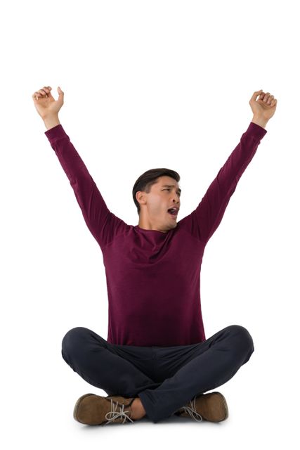 Businessman sitting cross-legged on floor, yawning with arms raised, wearing maroon shirt, black pants, and brown shoes. Ideal for concepts of fatigue, relaxation, work-life balance, office breaks, and casual business attire.