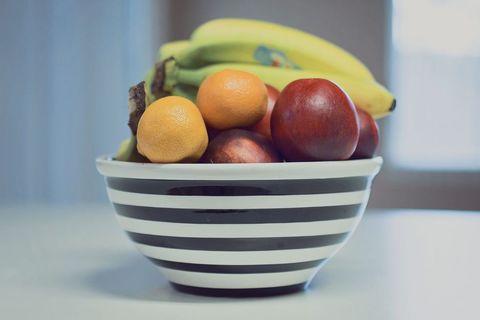 Displaying black and white striped bowl filled with bananas oranges and nectarines