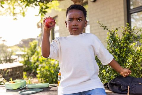 Determined african american boy holding red apple during outdoor school lunch break