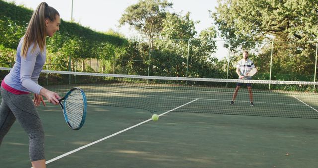 People playing tennis on an outdoor court. They are engaged in a friendly match, one ready to hit the ball and the other in a position ready to receive. Suitable for sports, outdoor activities, fitness and exercise concepts. Useful for health, sports equipment, and active lifestyle promotions.