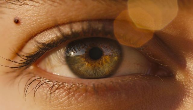 Hazel eye macro revealing detailed iris structure, long lashes and golden lens flare