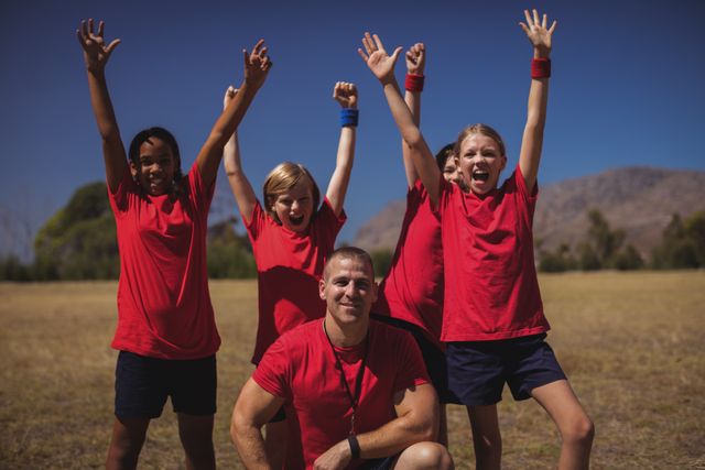 Group of children and their trainer celebrating success in an outdoor boot camp. Ideal for promoting teamwork, fitness programs, summer camps, and outdoor activities. Perfect for use in advertisements, brochures, and websites related to children's activities and fitness.