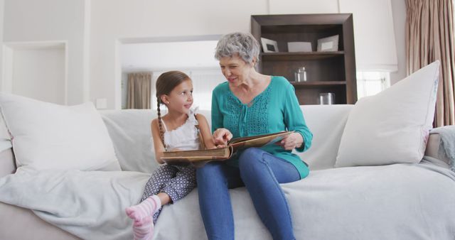 Happy caucasian grandmother and granddaughter sitting on sofa, looking at photo album - Download Free Stock Photos Pikwizard.com