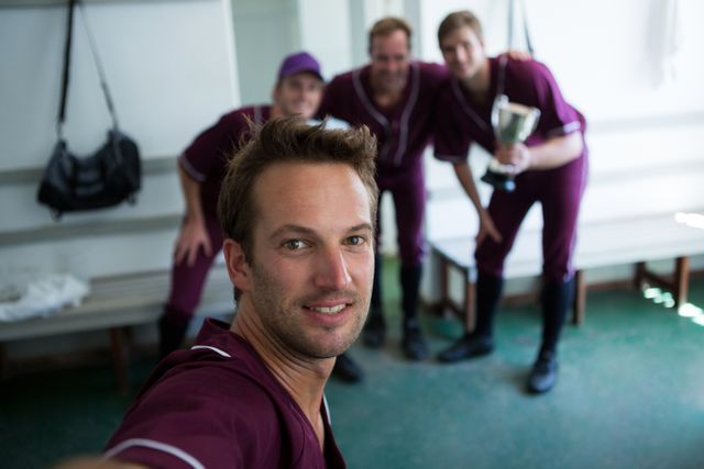 Portrait of smiling baseball team clicking selfie while standing at locker room after match