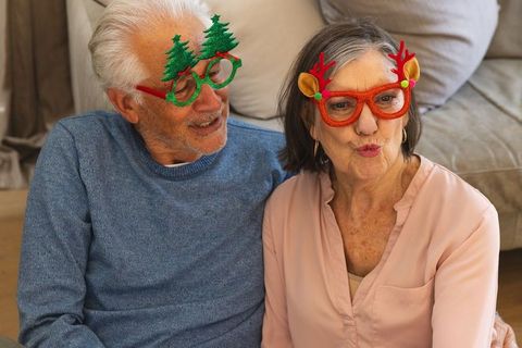 Cheerful senior couple displaying festive glasses in cozy living room