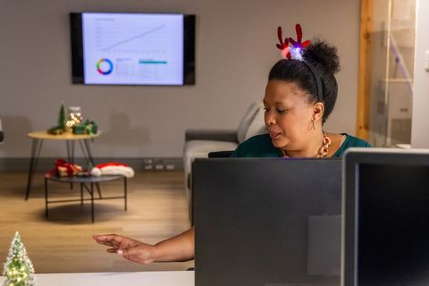 African american woman wearing led reindeer antlers working at dual-monitor office desk