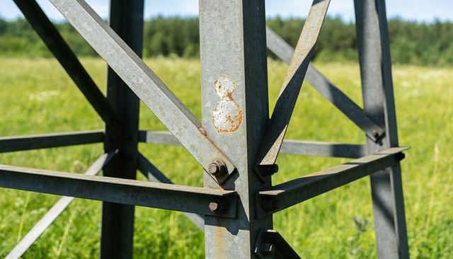 Weathered galvanized steel tower leg showing rusted bolts and bracing in rural meadow