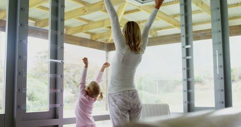 Mother and Daughter Standing Together with Raised Arms Indoors